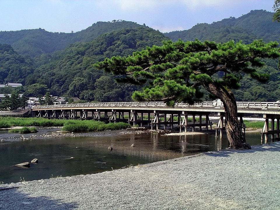 桂川に架かる渡月橋と川沿いの松、背後の山