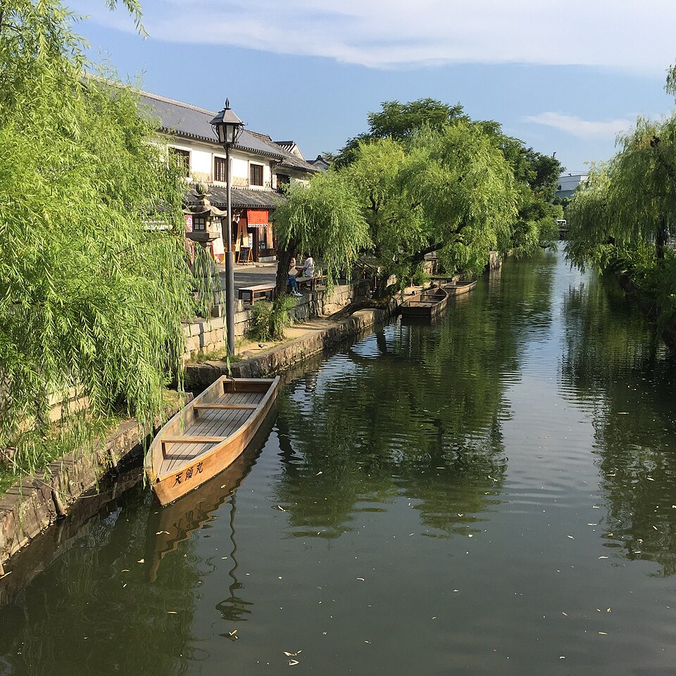 White-walled buildings and willow trees beside the Kurashiki canal, with wooden boats moored on the water